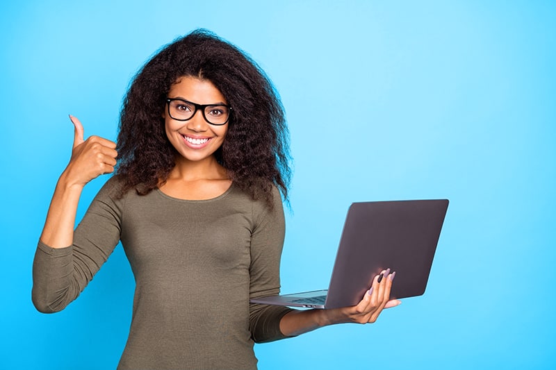 Una mujer joven confiada que sostiene una computadora portátil y sonriendo