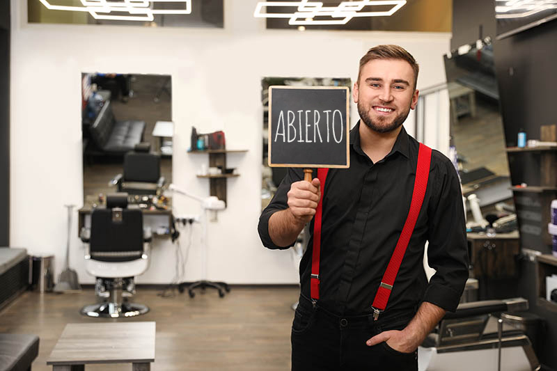 Un barbero joven y guapo con un cartel de "Abierto" en su peluquería